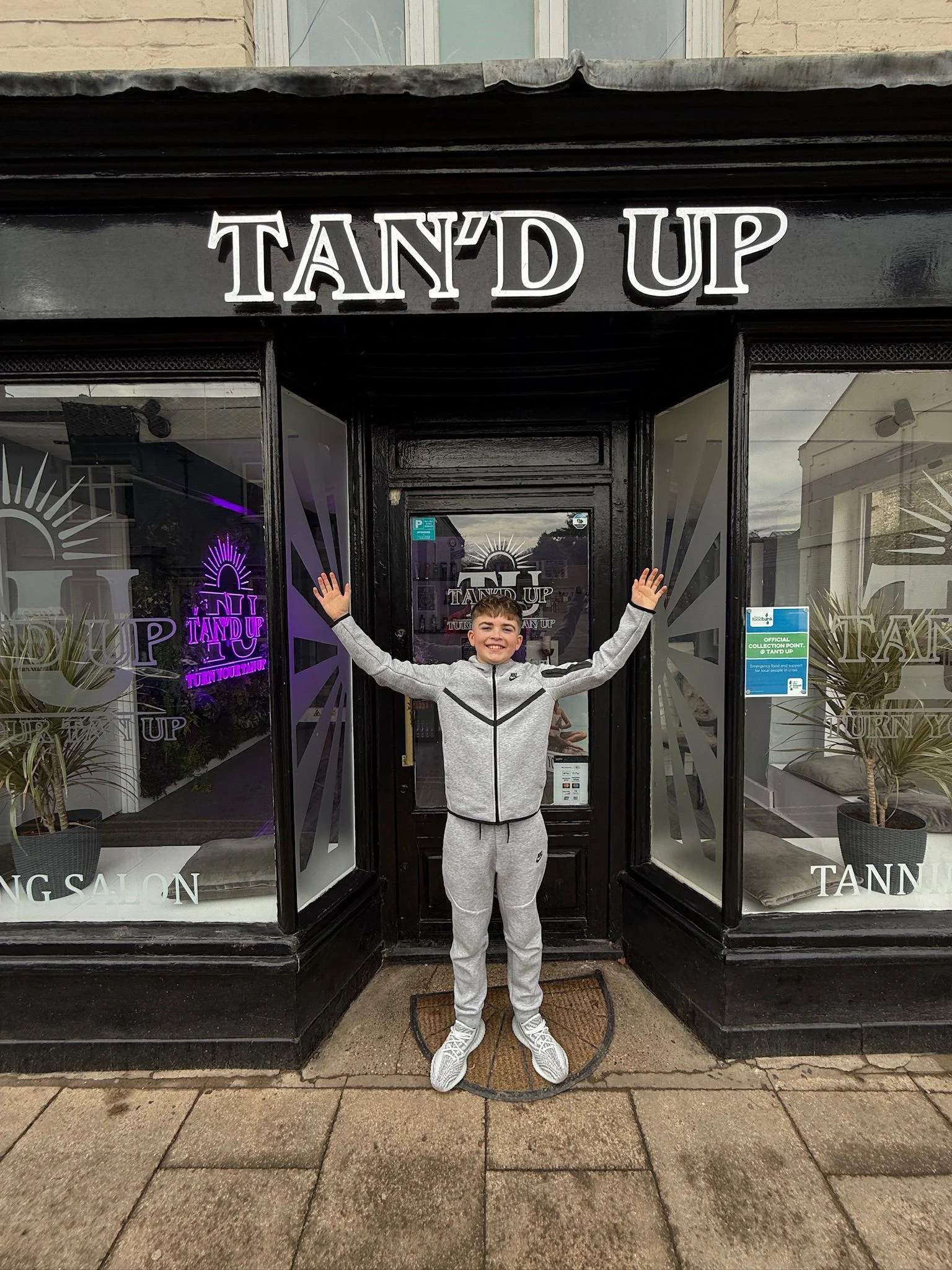 Kid standing happy in front of some store called Tan'd Up